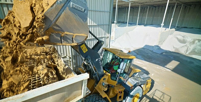 A construction loader unloading sand into a hopper at an industrial site